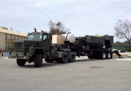 Front view of volumetric concrete mixing truck on job site - government property. Volumetric mixer is painted in military color and chute is down ready to pour.