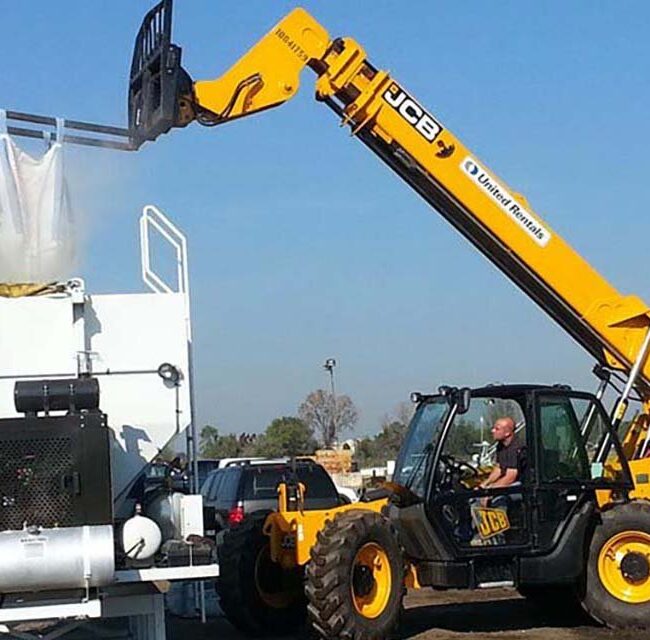 A customized volumetric concrete mixing truck being loaded by a concrete company at a batching plant.