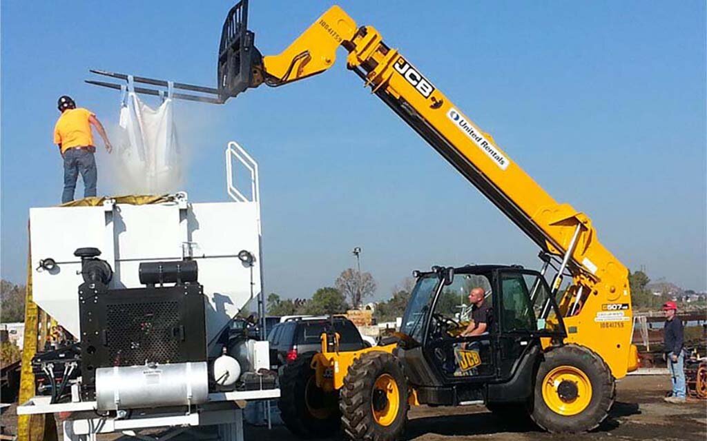 A customized volumetric concrete mixing truck being loaded by a concrete company at a batching plant.
