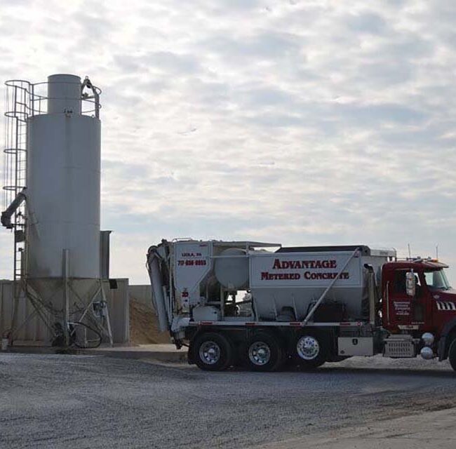 A volumetric concrete mixing truck parked next to a cement silo ready for batching.