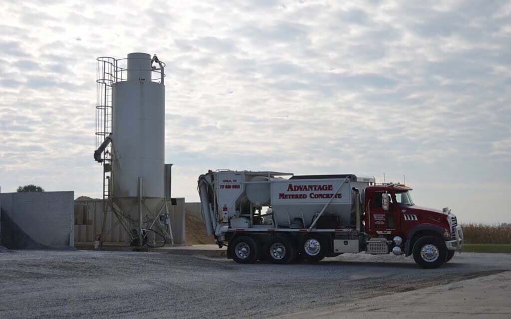 A volumetric concrete mixing truck parked next to a cement silo ready for batching.