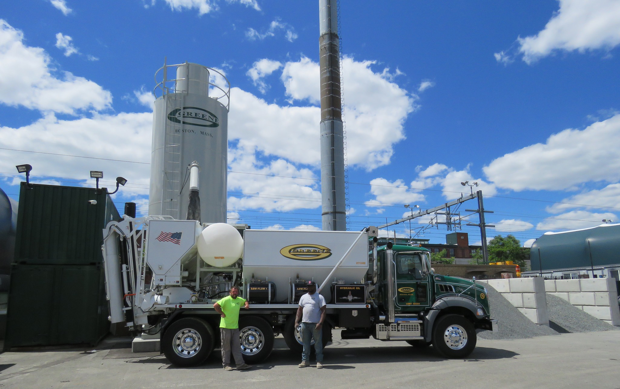 Volumetric concrete mixing truck is on job site parked in front of a round portable cement silo. The truck is ready to be loaded at the batching plant for on-site mixing for a fresh concrete pour.