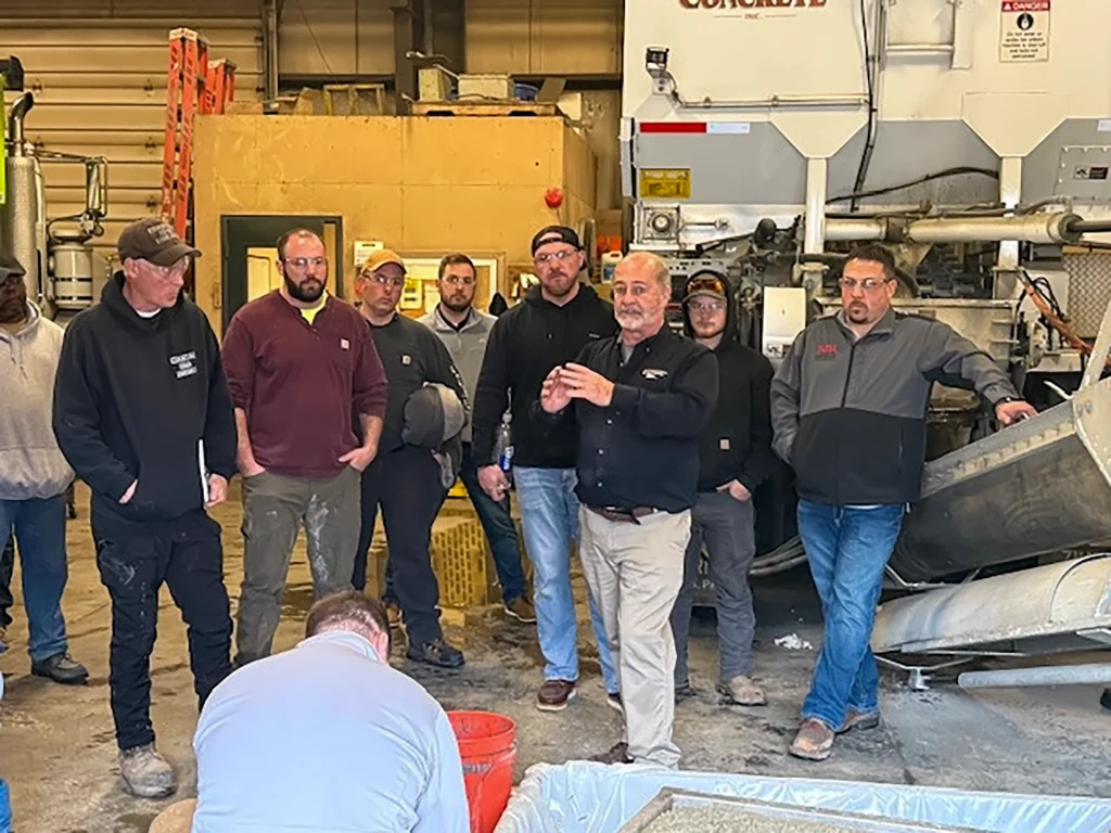 Zimmerman Industries, Inc. offering National Ready-Mix Concrete Association (NRMCA)vaccredited training courses to Zim-Mixer owners, covering topics such as calibration, operation and basic maintenance for service and parts. Trainer is instructing while students follow behind him.